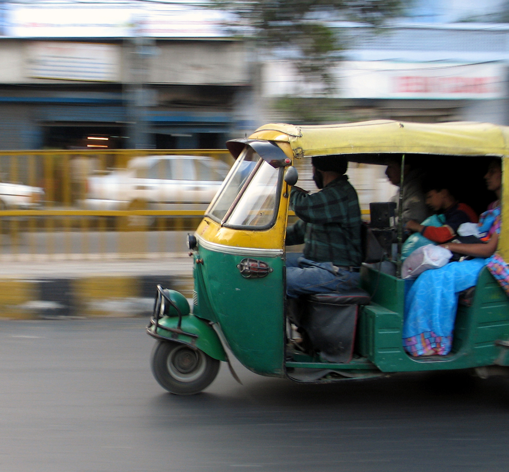 A green and yellow motorized rickshaw zips through the streets of Delhi, India.