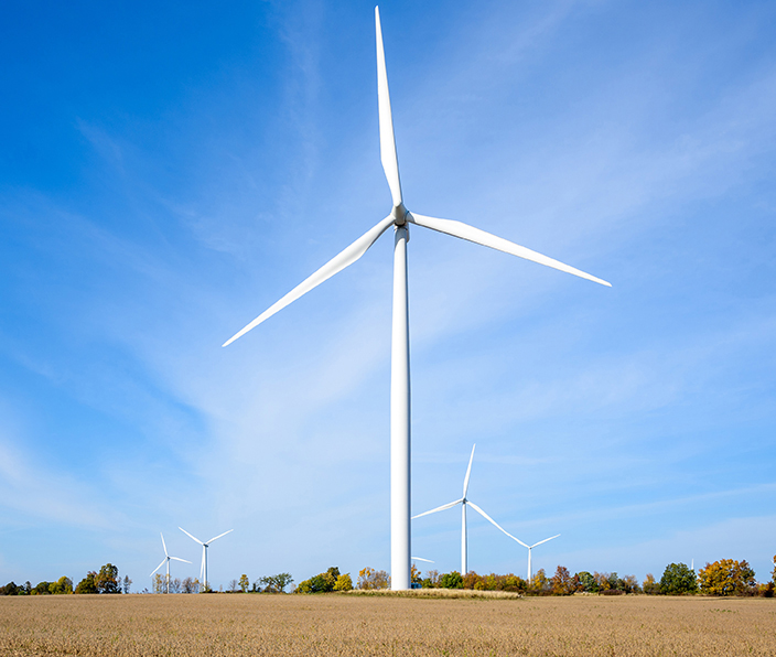 Tall wind turbines in a wheat field under blue sky in autumn.