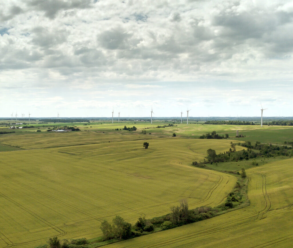 Tall wind turbines in the distance on a field under cloudy sky, ON, Canada.